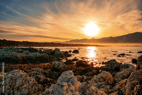 Dramatic orange cloudscape sunset at dusk over the rocks and bay at Kaikoura harbour