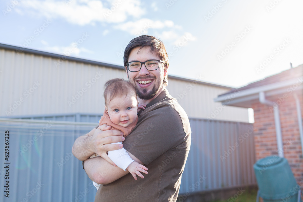 Young father in his twenties holding his baby outside in backyard of home Young father in his twenties holding his baby outside in backyard of home