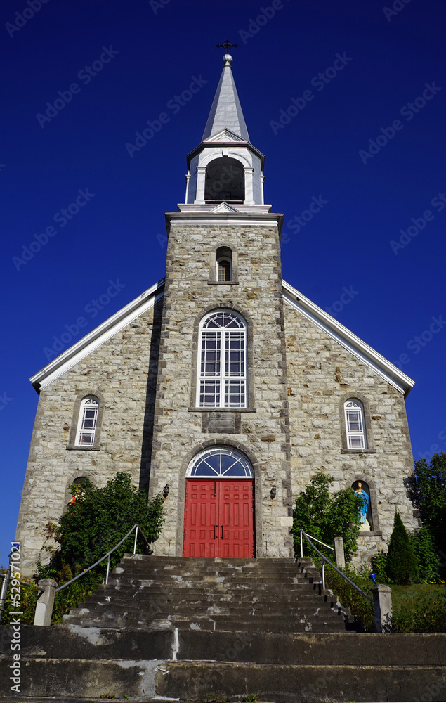 Facade and steeple of an old stone Roman Catholic church in a village in western Quebec