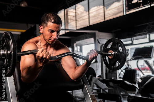 High quality photography. Muscular Latino man without a shirt in a gym training Man training with a barbell.