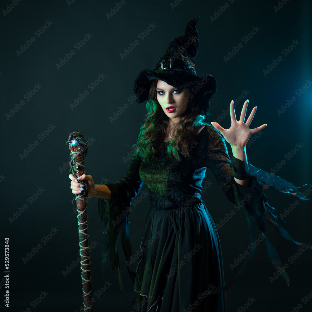 A witch with a staff sends a spell. Young witch in black dress and pointed hat, Halloween image