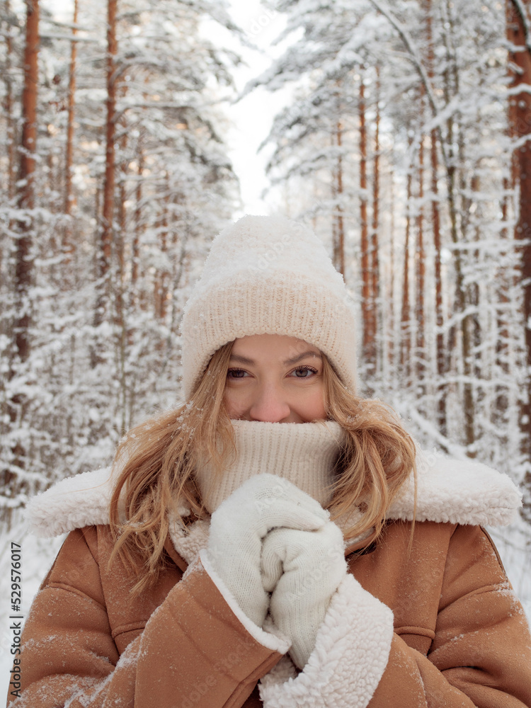 Winter walk a young beautiful blonde in winter clothes walking in a snowy forest a beautiful frosty day. A young woman warms her nose wrapped in a white scarf Stock Photo
