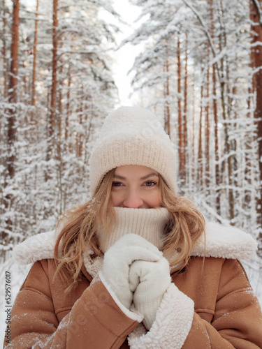 Winter walk, a young beautiful blonde in winter clothes walking in a snowy forest, a beautiful frosty day. A young woman warms her nose wrapped in a white scarf © Ulia Koltyrina