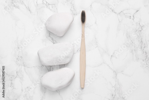 Eco toothbrush with white pebble stones on a marble background. Natural composition. Dental care. Top view