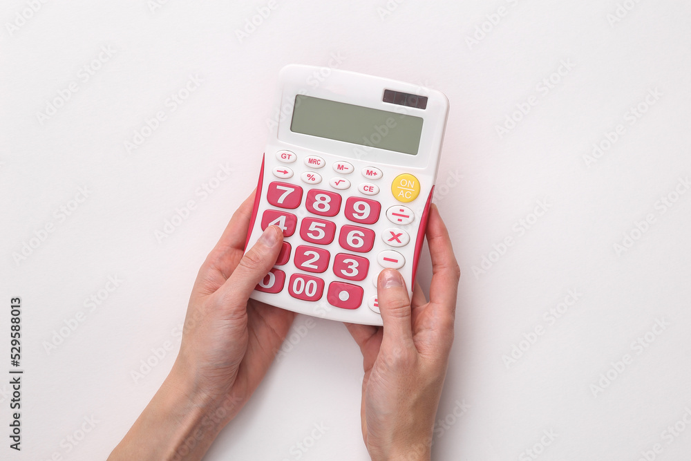 Female hands hold a white calculator with pink buttons on a gray background Female hands hold a white calculator with pink buttons on a gray background