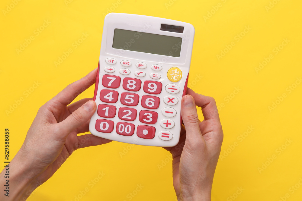 Female hands hold a white calculator with pink buttons on a yellow background Female hands hold a white calculator with pink buttons on a yellow background