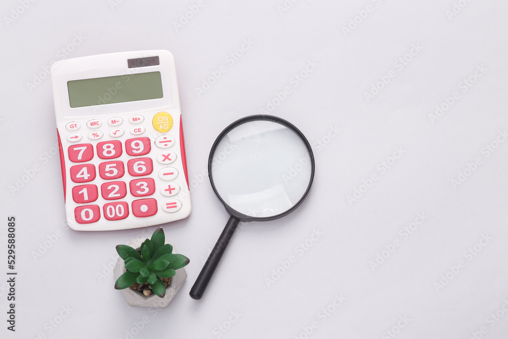 Calculator with magnifying glass and decorative plant on a gray background. Business concept. Copy space Calculator with magnifying glass and decorative plant on a gray background. Business concept. Copy space