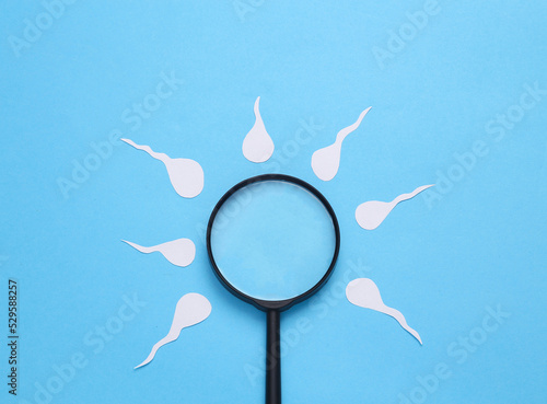 Diagnosis of male reproductive function. Spermatozoa, male seed with a magnifying glass on a blue background