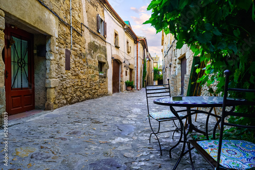 Nice alley full of stone houses and iron table and chairs to rest, Peratallada, Girona, Spain. © josemiguelsangar