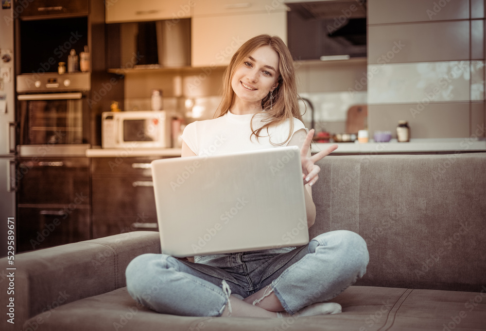 Young cute smiling woman with laptop looking at camera while sitting on sofa in living room Young cute smiling woman with laptop looking at camera while sitting on sofa in living room