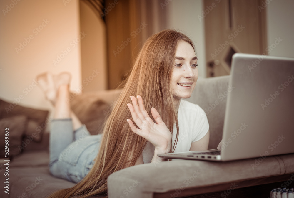 Young cute woman communicating by video call with laptop while lies on sofa in living room Young cute woman communicating by video call with laptop while lies on sofa in living room