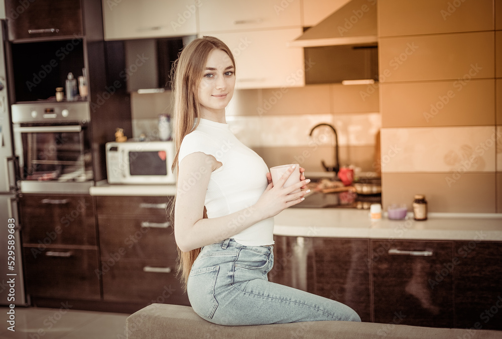 Cute young woman with a cup of coffee or tea in living room Cute young woman with a cup of coffee or tea in living room