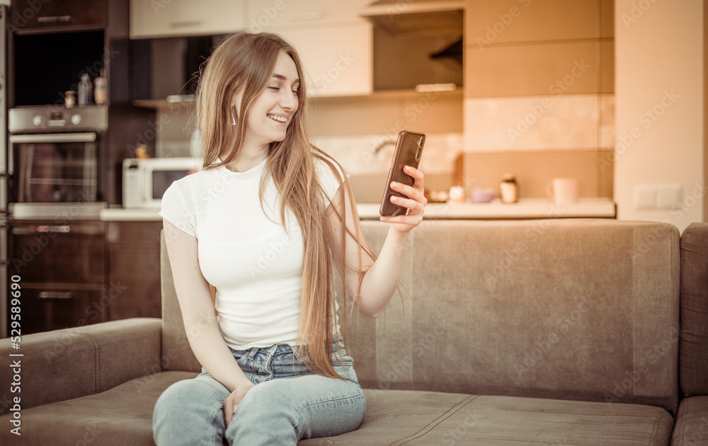 Cute young woman looking at smartphone screen while sitting on sofa in living room Cute young woman looking at smartphone screen while sitting on sofa in living room