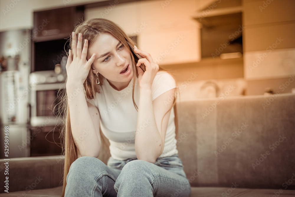 Puzzled woman talking on the phone while sitting on the sofa in the living room