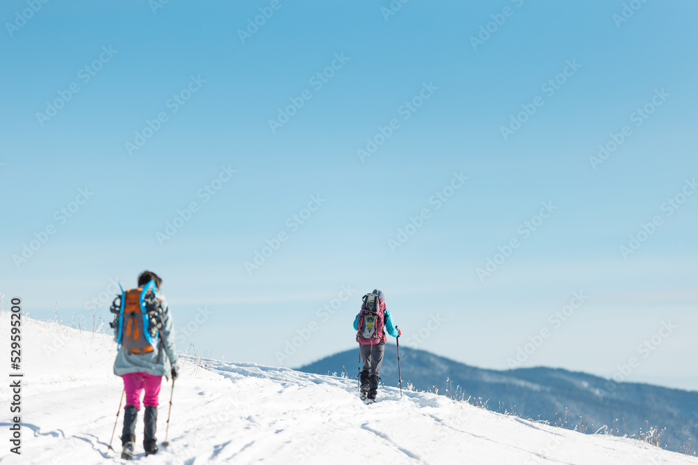 two girls with backpacks walk along a path in the winter mountains. hiking in the mountains.