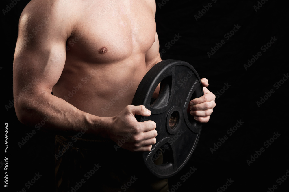 the torso of a strong man with a barbell disk in his hands, the background is dark. dark key photography the torso of a strong man with a barbell disk in his hands, the background is dark. dark key photography