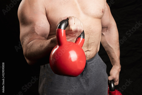 torso of a man with a red kettlebell in his hands, an athlete with muscles on a dark background
