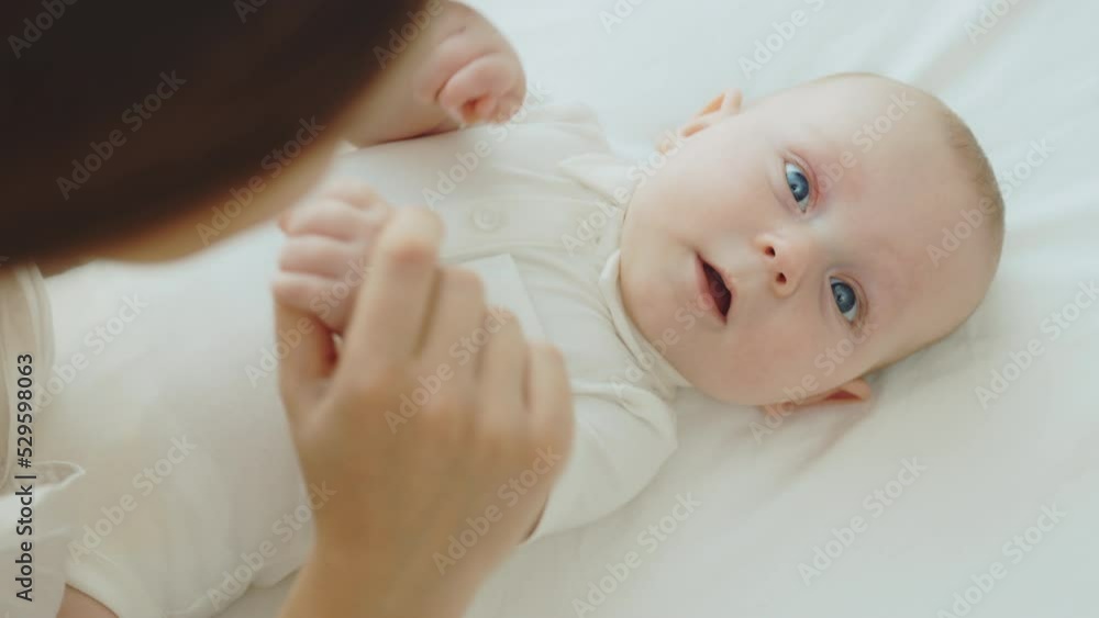 Top view of mother playing with her newborn baby. Caring mom and neonate toddler together at home. Litthe human looking at camera. Concept of childhood, motherhood and new life Top view of mother playing with her newborn baby. Caring mom and neonate toddler together at home. Litthe human looking at camera. Concept of childhood, motherhood and new life