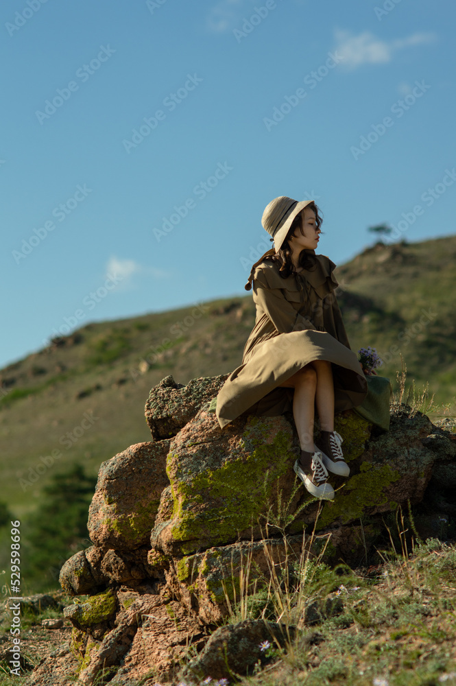 Naklejka premium young lady sitting on the stone against the blue sky and the wind plays with the hem of the dress on the blurred background
