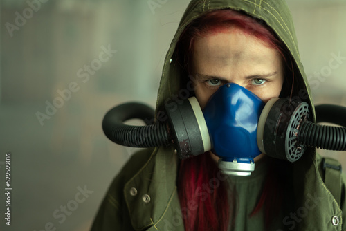 Young pandemic survivalist woman in gas mask looking in front of her on the background with apocalyptic war area around. Sad woman in breathing oxy mask photo