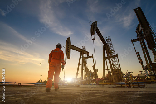 Silhouette of oil workers working in oil rig or oil fields and gas station in the evening with beautiful sunset.