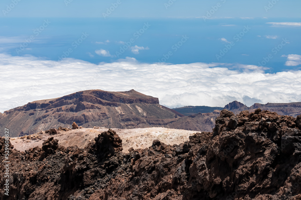 Obraz premium Scenic view from summit of volcano Pico del Teide over the island of Tenerife, Canary Islands, Spain, Europe. Vista on barren landscape, solidified lava, ash, pumice. Valley and sea covered in clouds
