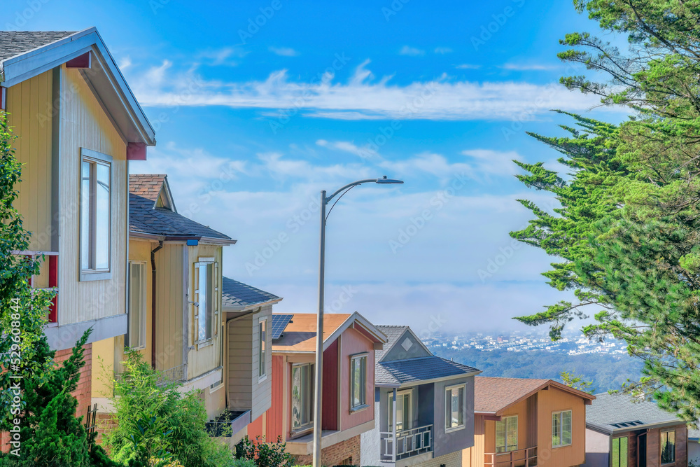 Row of houses on a sunlit street against blue sky and clouds on a sunny day Row of houses on a sunlit street against blue sky and clouds on a sunny day