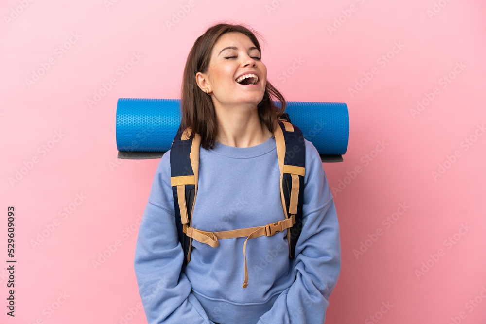 Young mountaineer woman with a big backpack isolated on pink background laughing Young mountaineer woman with a big backpack isolated on pink background laughing