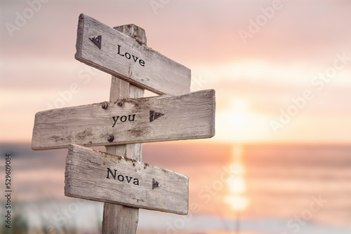 love you nova written on wooden signpost outdoors on the beach with romatic sunset in the back. Power words and popular name concept.