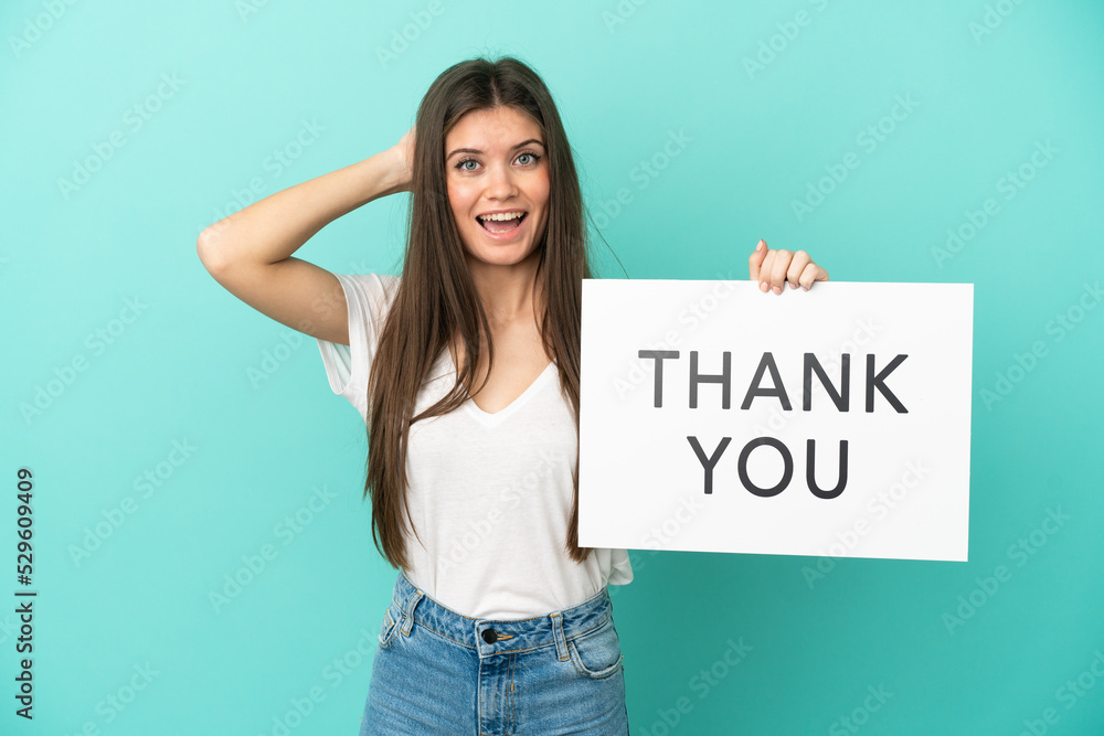 Young caucasian woman isolated on blue background holding a placard with text THANK YOU with surprised expression Young caucasian woman isolated on blue background holding a placard with text THANK YOU with surprised expression