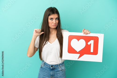 Young caucasian woman isolated on blue background holding a placard with Like icon with proud gesture