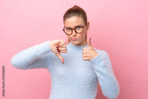 Young caucasian woman isolated on pink background making good-bad sign. Undecided between yes or not photo