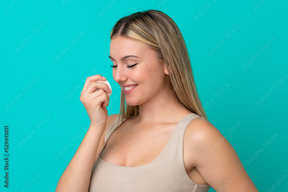 Young caucasian woman isolated on blue background with moisturizer and smelling it Young caucasian woman isolated on blue background with moisturizer and smelling it