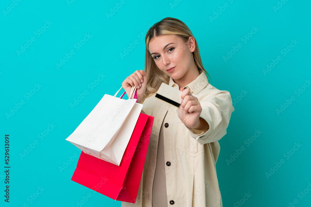 Young caucasian woman isolated on blue background holding shopping bags and a credit card Young caucasian woman isolated on blue background holding shopping bags and a credit card