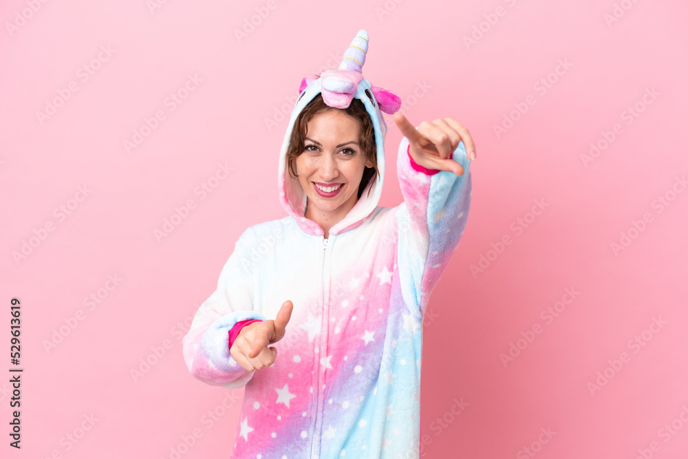 Young caucasian woman with unicorn pajamas isolated on pink background points finger at you while smiling