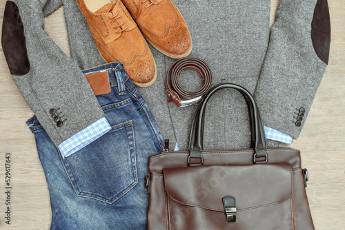 A pair of brown suede derby shoes, blue jeans, leather and bag belt with grey tweed blazer. Casual business outlook. Top view.