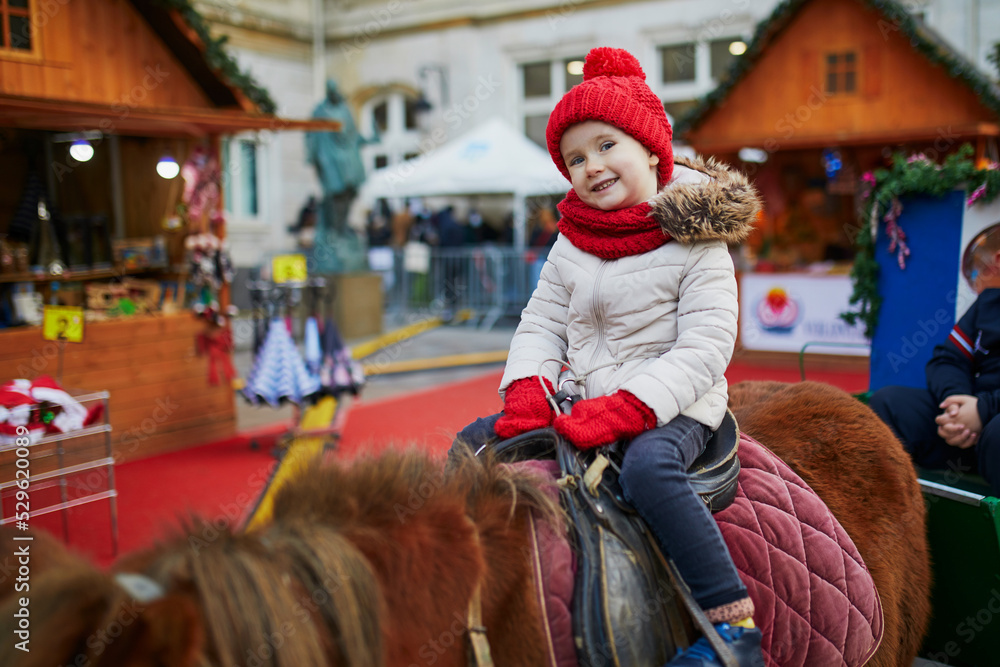 Happy cheerful preschooler girl on a Christmas market in Paris, France