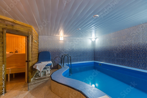 The interior of the health center with a sauna, a blue pool and a massage table. © alhim