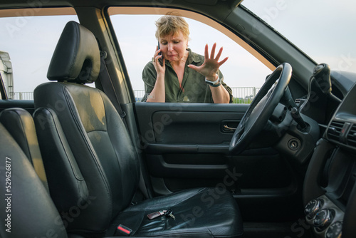 Middle-aged woman looks through the glass into the interior of her car with the keys in the driver's seat. Woman driver forgot her keys in the car and calling technical assistance