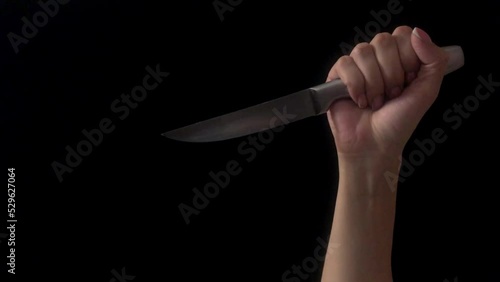 Human hand with knife shot on a black background. Woman's hand holds knife. The hand makes stabs with a knife. Concept of violence, murder with kitchen knife
