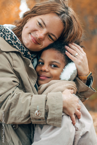 Happy multiracial mom and daughter hug in the autumn park.Diverse people,autumn concept.