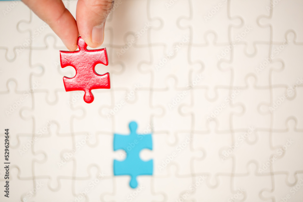 Close up hand holding and playing jigsaw game incomplete. White part of jigsaw puzzle pieces on blue background. concepts of problem solving, business, teamwork. Close up hand holding and playing jigsaw game incomplete. White part of jigsaw puzzle pieces on blue background. concepts of problem solving, business, teamwork.