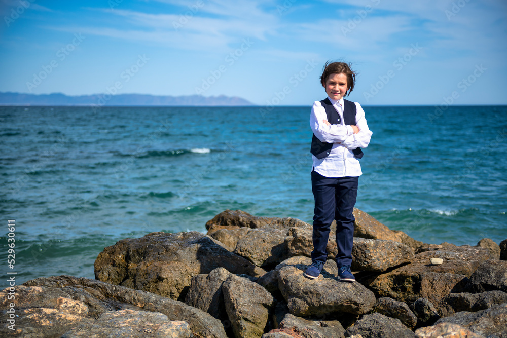 child poses on rocks with sea in background