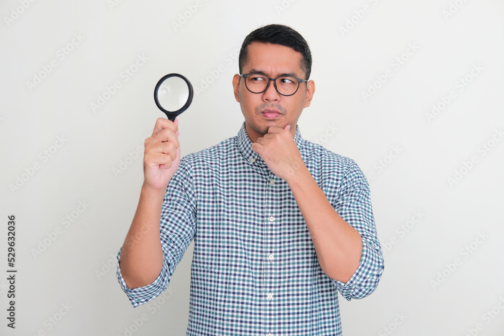 Asian man holding magnifying glass with curious face expression