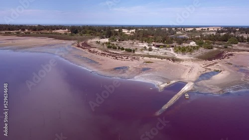 Aerial footage of pink lake full of salt with dry shore, clouds reflecting on the lake and ocean in background, Retba lake, Dakar, Senegal, going sideway along shore while panning. photo