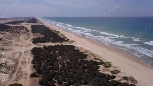 Aerial footage of ATV or quads driving along huge beach with bushes on top, ocean waves are crashing in background, Retba lake, Dakar, Senegal, going sideway towards land. photo