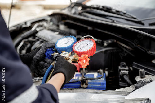 Close up hand of auto mechanic using measuring manifold gauge check the refrigerant and filling car air conditioner for fix and checking for repair service support maintenance and car insurance.