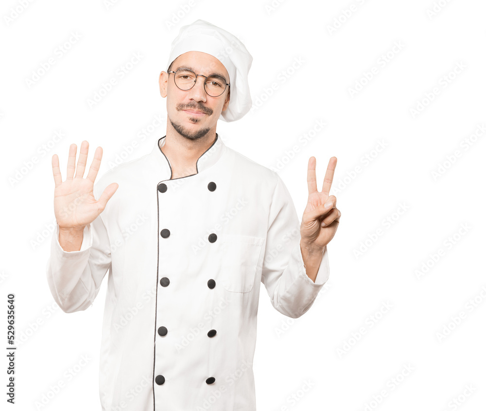 Happy young chef doing a number seven gesture with his hands Happy young chef doing a number seven gesture with his hands