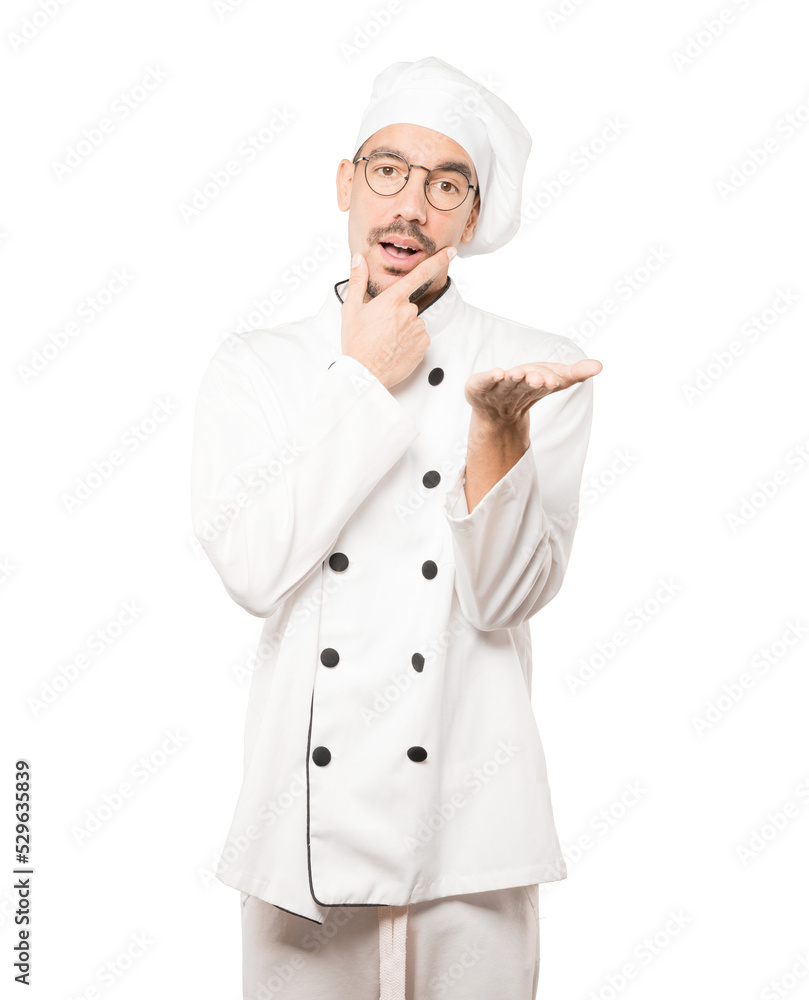 Doubtful young chef holding something with his hand Doubtful young chef holding something with his hand