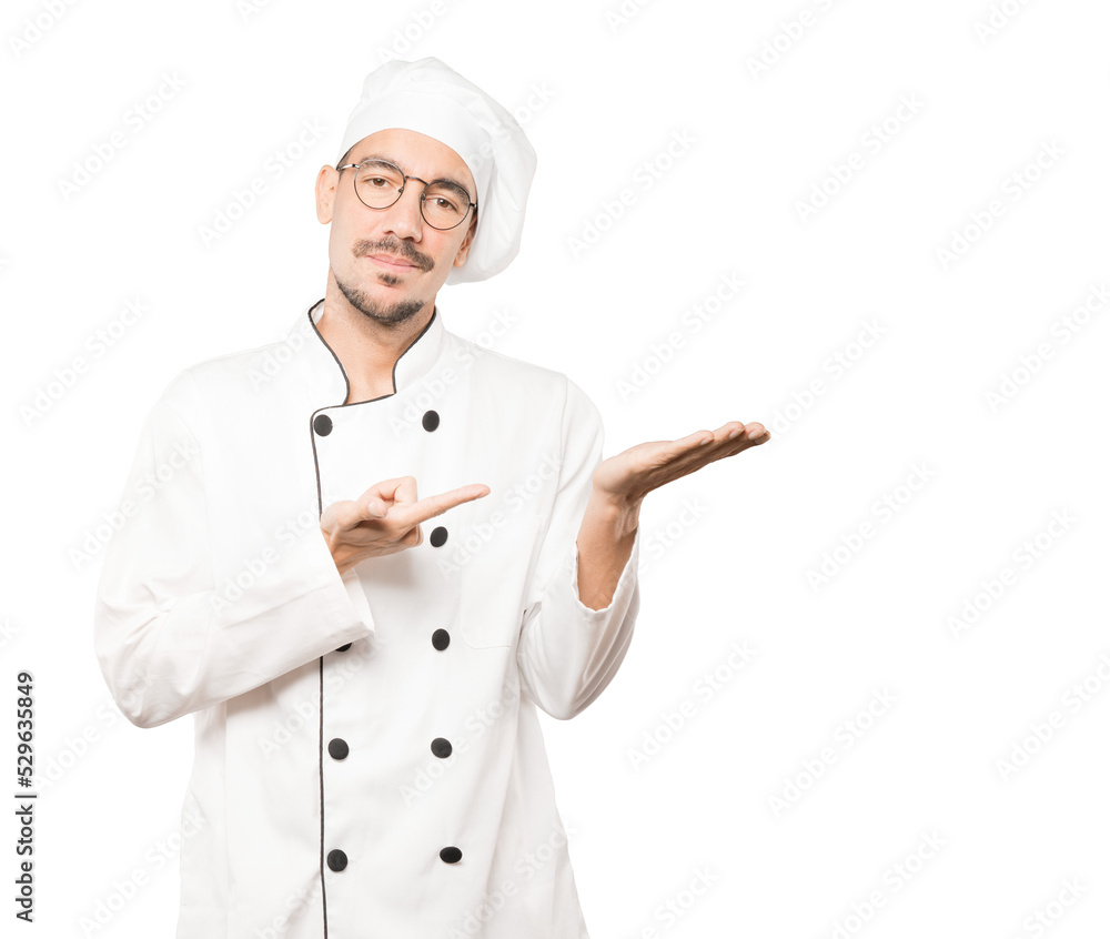 Doubtful young chef holding something with his hand Doubtful young chef holding something with his hand